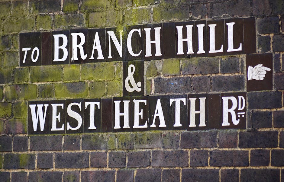 Photograph of a brick wall featuring a street sign with black and white tiles. The sign reads