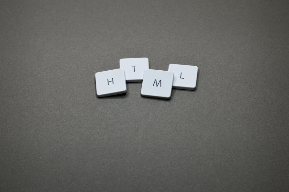 A close-up image of four small white lettered tiles arranged on a grey textured surface, spelling 'H T M L'. The tiles are made of plastic or similar material, each featuring a single black letter on